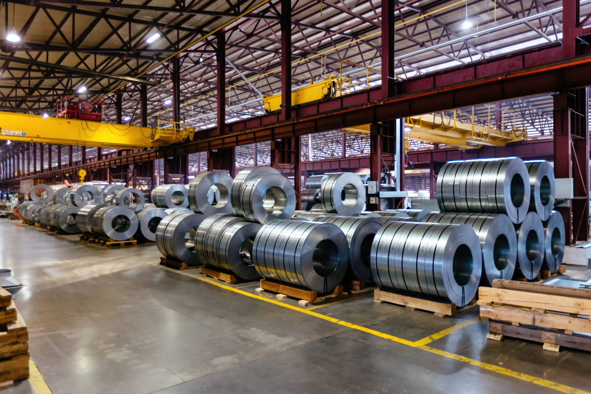 Usine industrielle avec rouleaux d'acier empilés et pont roulant jaune — site de production à forte intensité énergétique